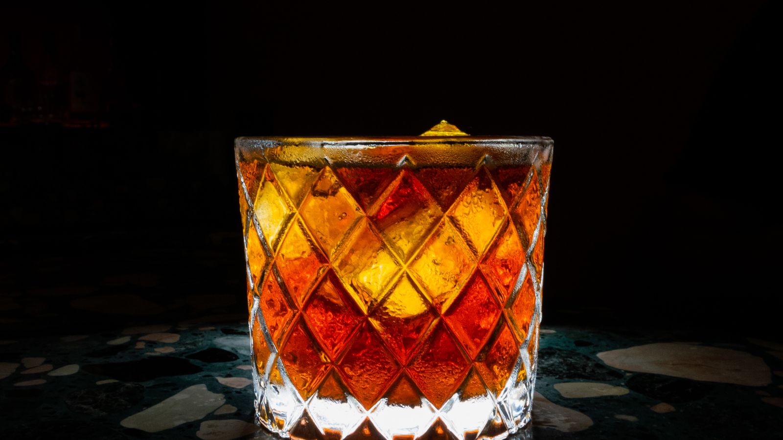 Illustrative amber cocktail in a crystal glass against a dark studio background.