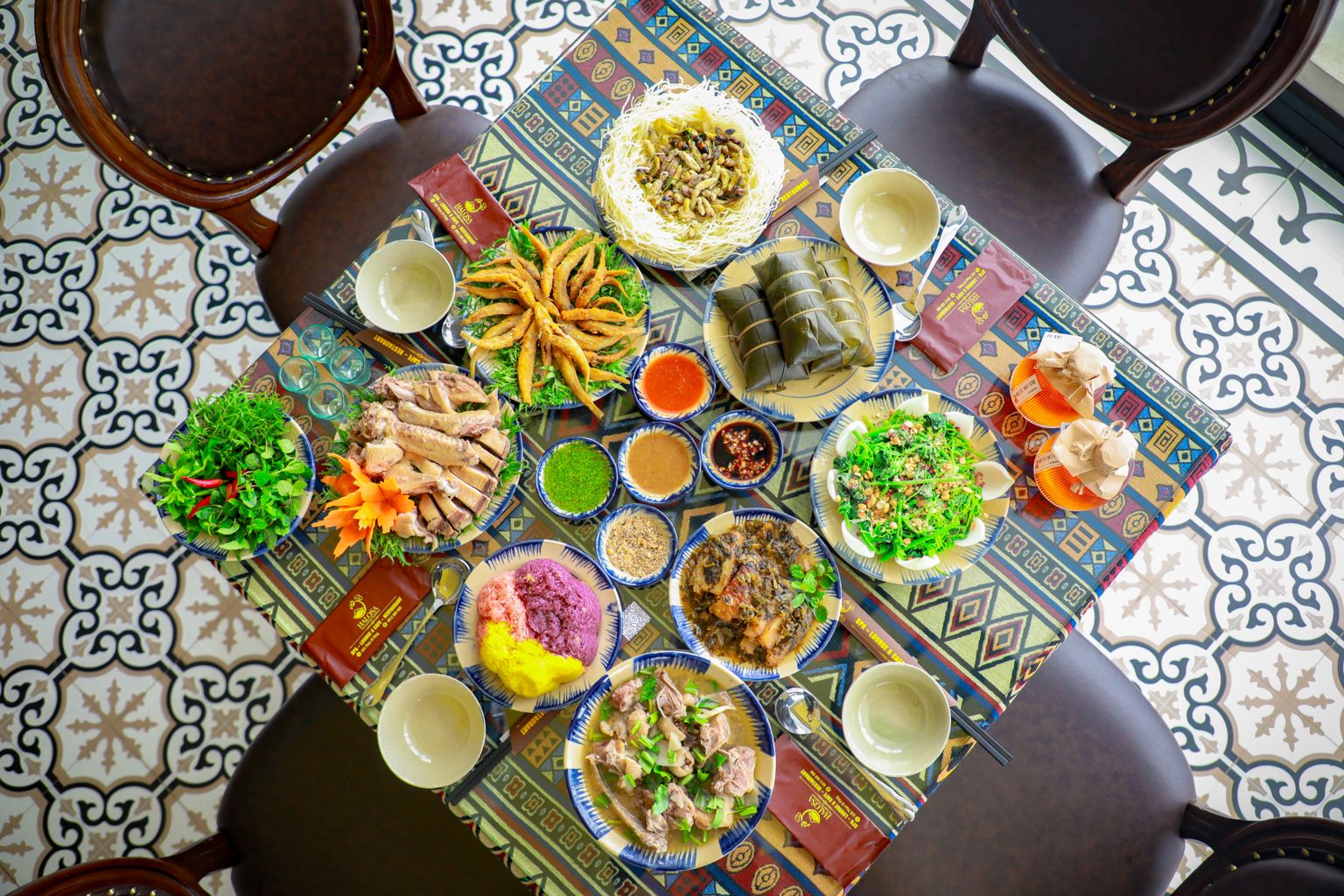 Illustrative overhead view of diverse Asian dishes on a colorful tablecloth, representing a dining-led evening in Ho Chi Minh City.