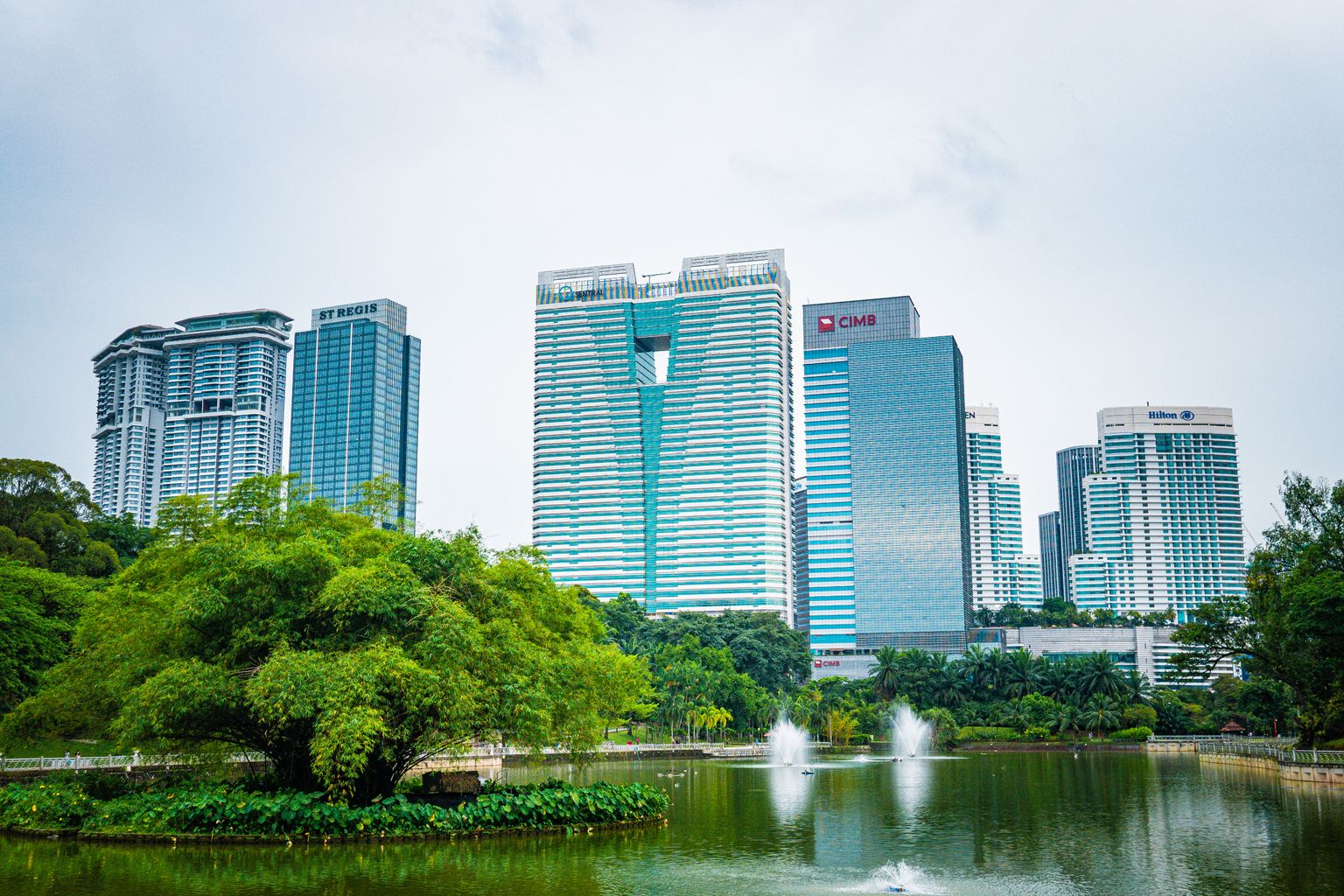 Kuala Lumpur skyline beyond a green urban park and water fountain in daylight