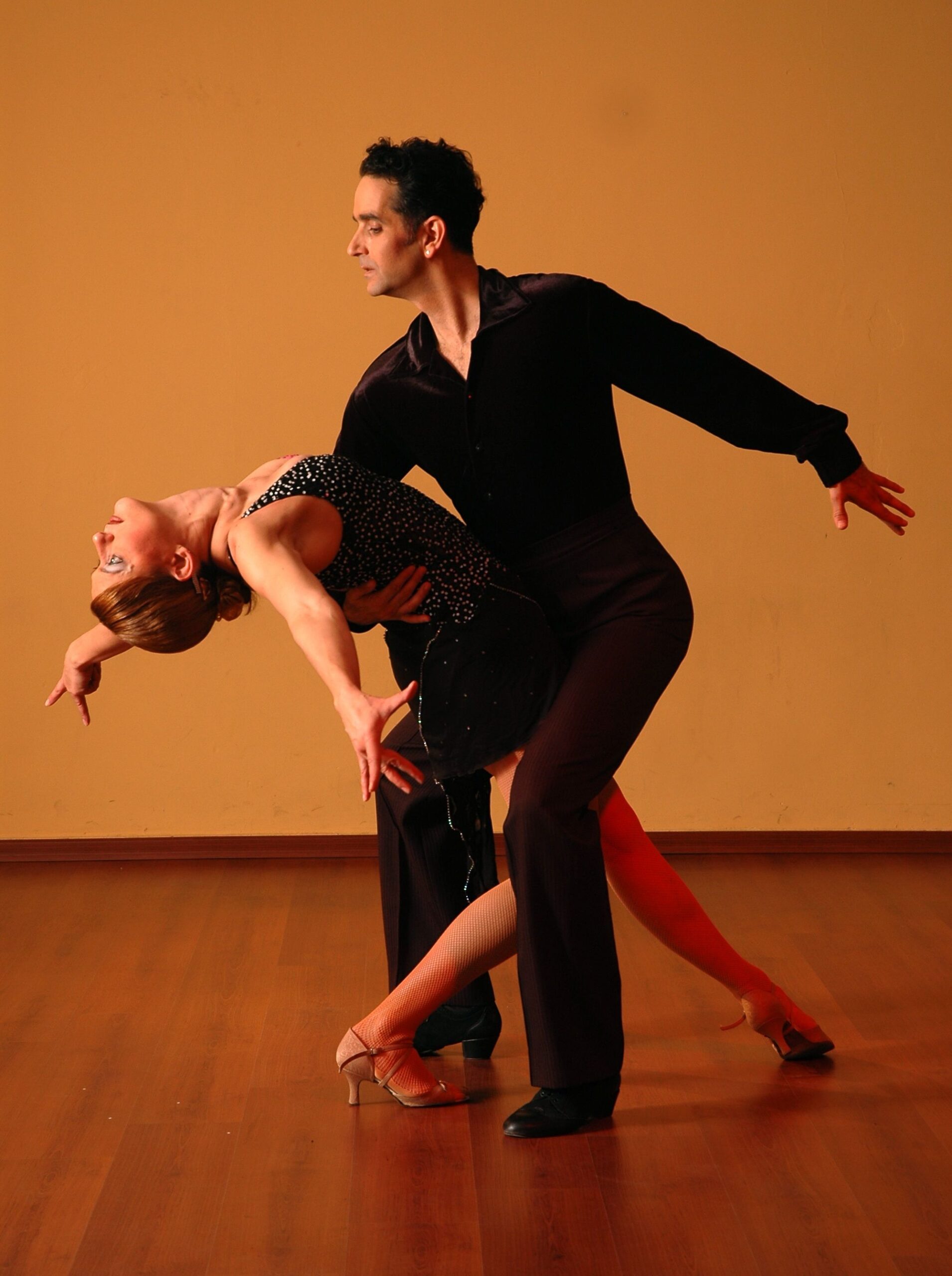 Illustrative ballroom dancers performing on a wooden floor.