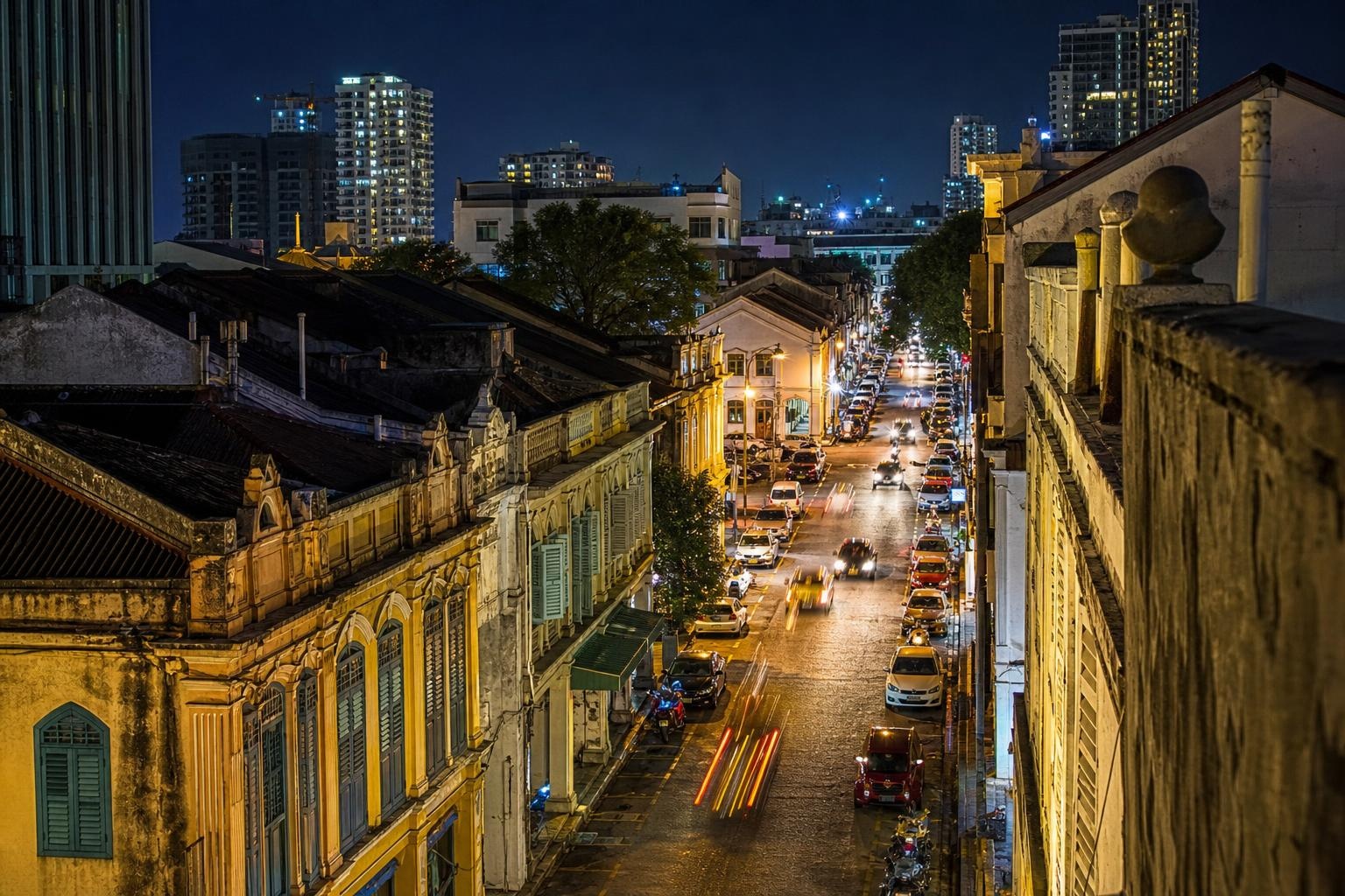 Illustrative night view of a historic George Town street in Penang with traffic and illuminated buildings.