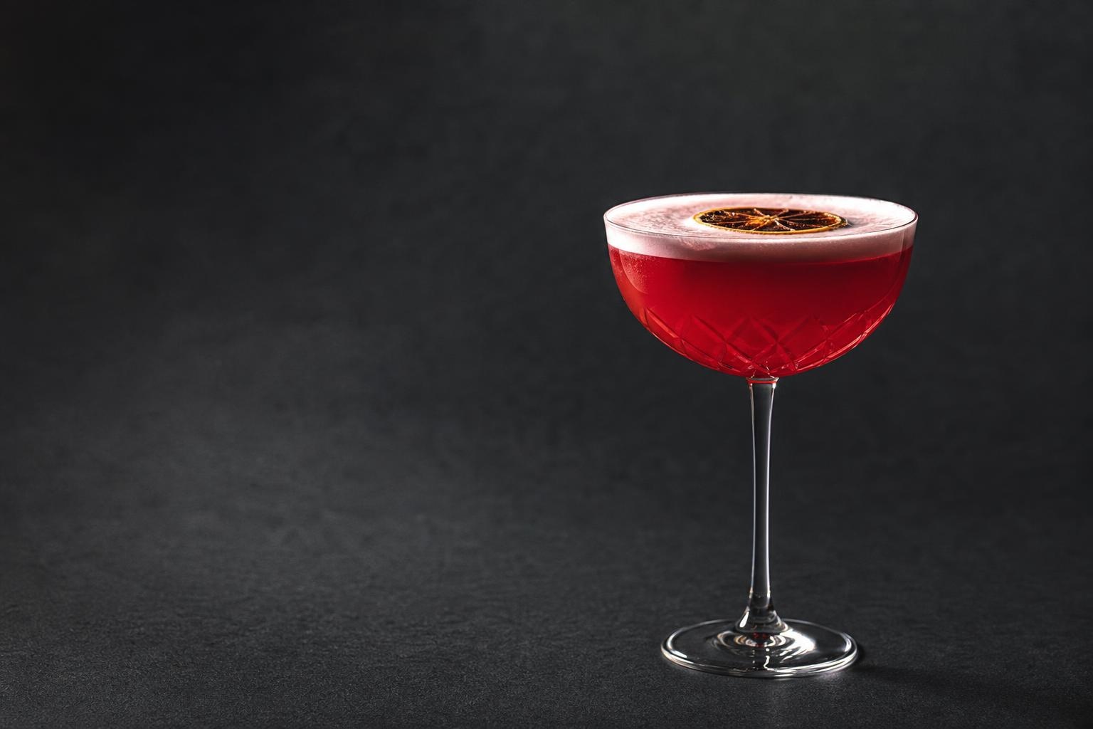 Illustrative red cocktail in a coupe glass against a dark studio background, with no rooftop venue shown.